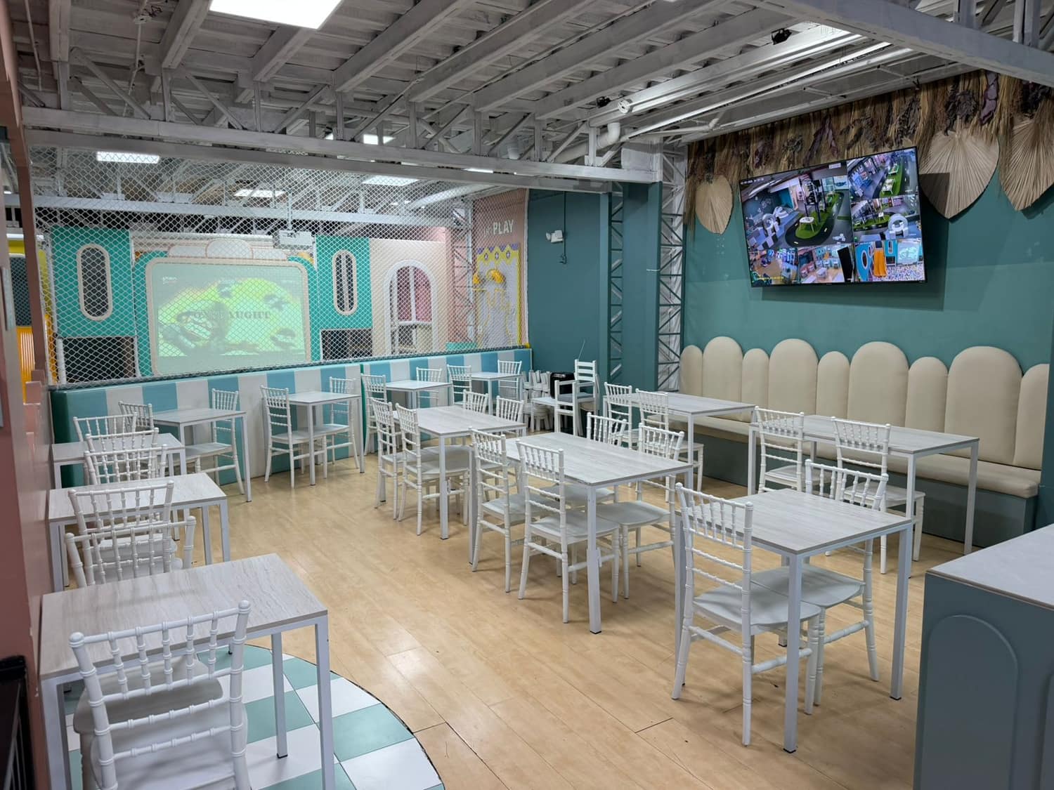 Zona de mesas de la cafetería con pantallas para ver a los niños